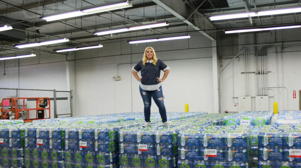 A woman in denim pants standing on top of many cases of water in a warehouse