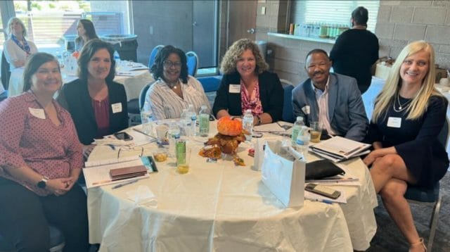 Five people sitting and smiling at a table at a leadership conference.
