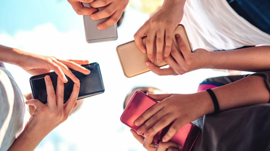 Four young people holding mobile phones with blue sky in the background.