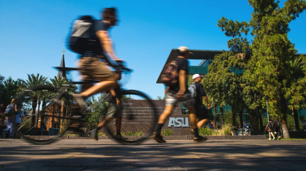A person on a bicycle, an ASU logo and green trees in the background