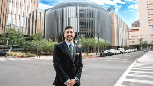A person in a suit standing in front of the Thunderbird School for Global Management building at ASU