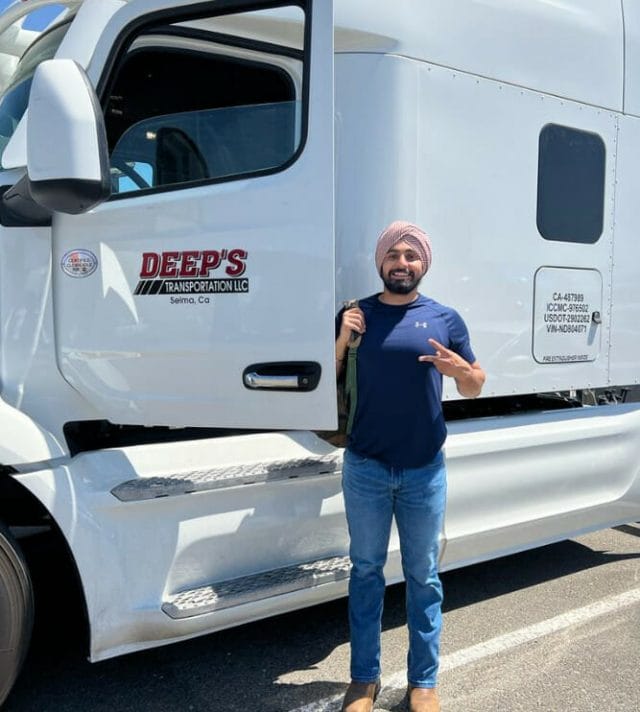 A person poses for a photo in front of a large white freight vehicle. 