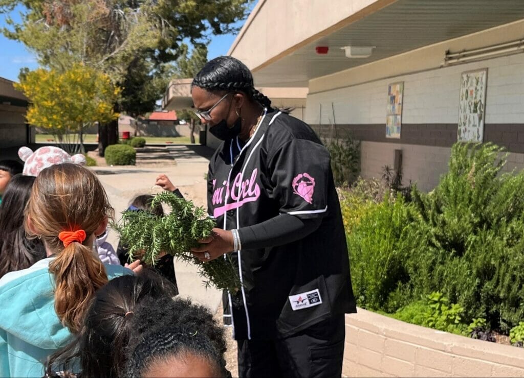 A woman in a black shirt holding a plant and interacting with children outdoors