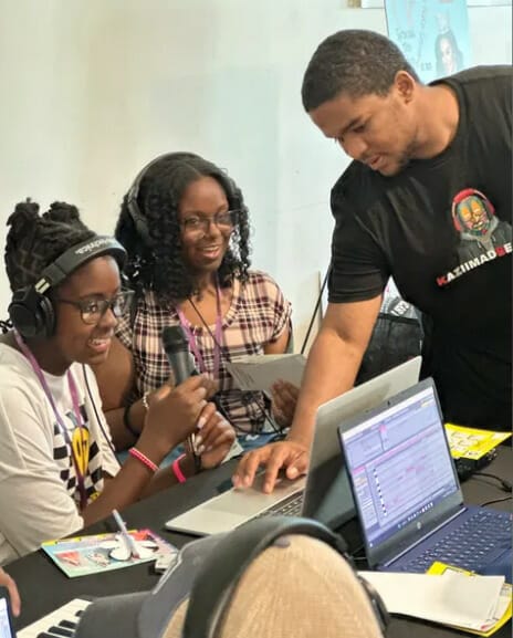 Three young people with headphones on and laptops working together