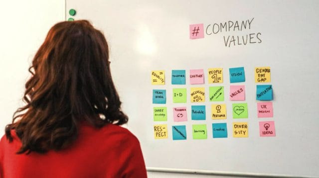 A person in a red sweater looking at a white board with colorful sticky notes on it