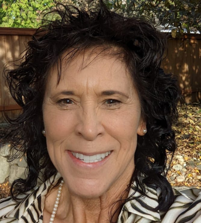 A person with dark hair smiling with a residential yard in the background.