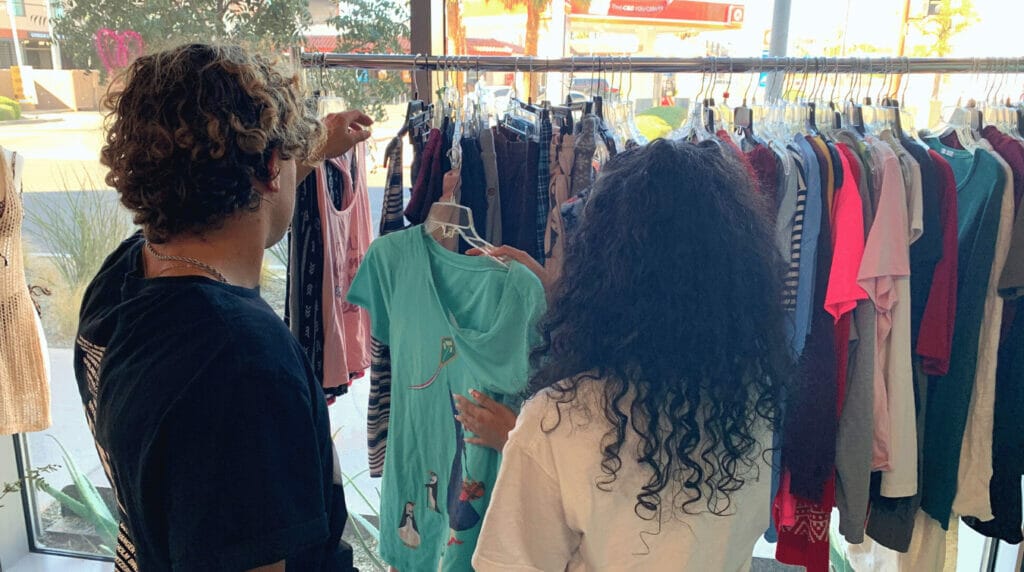 Two people standing in front of a clothing rack and looking at a colorful blouse