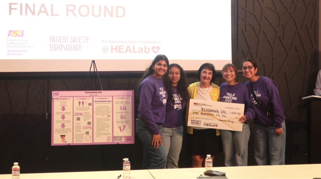 Five people smiling and holding a large check with a black wall behind them