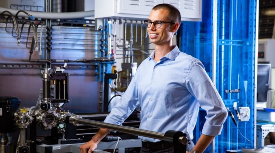 A person smiling, wearing glasses, and standing within a high tech machine