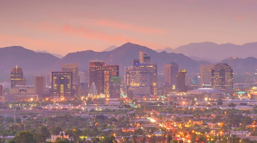 A distant view of city buildings with lights in the evening with mountains in the background