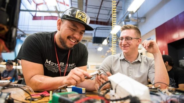 Two people smiling and working together in a makers space with wires covering a table