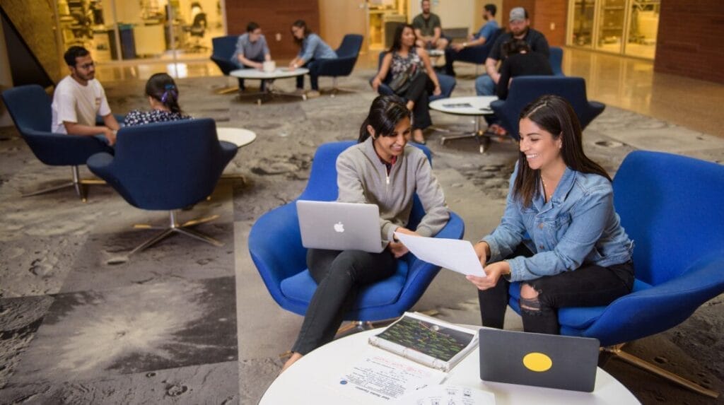 An indoor area with students sitting on blue modern style chairs collaborating with each other