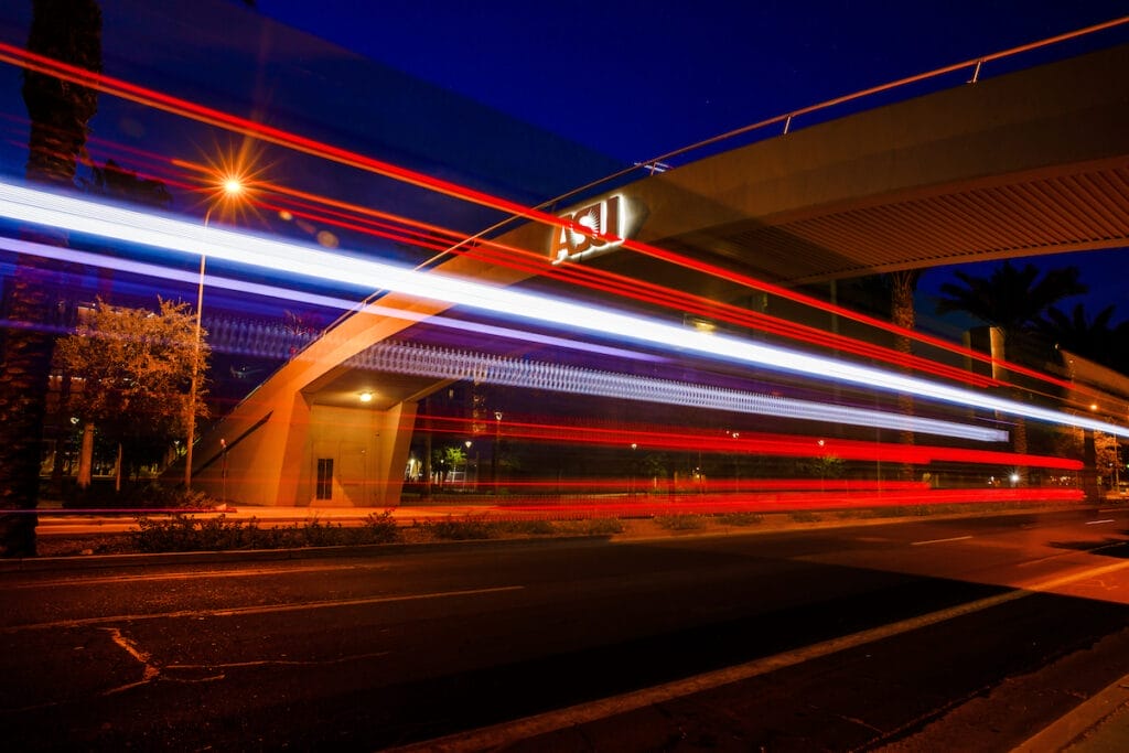 A night view of a bridge over a street with the ASU logo on it and bright streaks of light across the photo 

