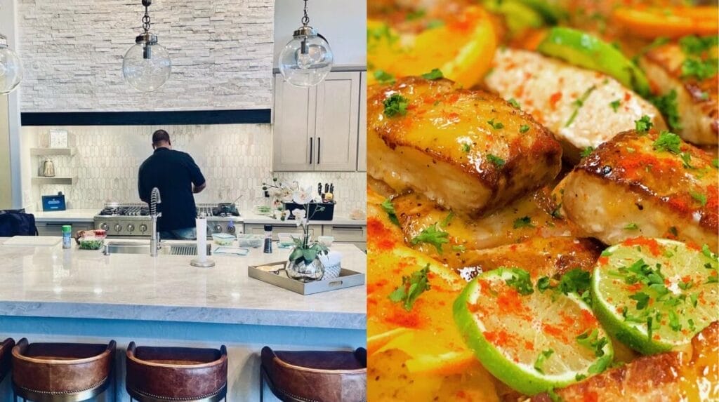 A back view of a person cooking in a kitchen with white counters and leather stools and a grilled fish dish with lime slices.
