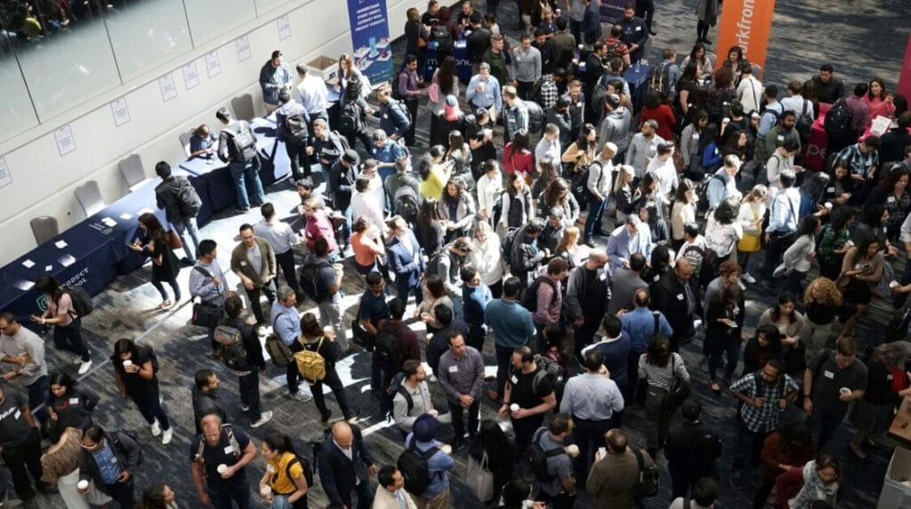 A large group of people standing in a large hall at a professional event
