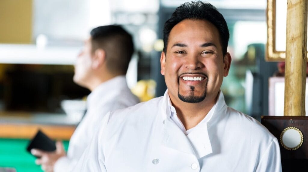 Restaurant owner wearing a white chef jacket smiling at his restaurant