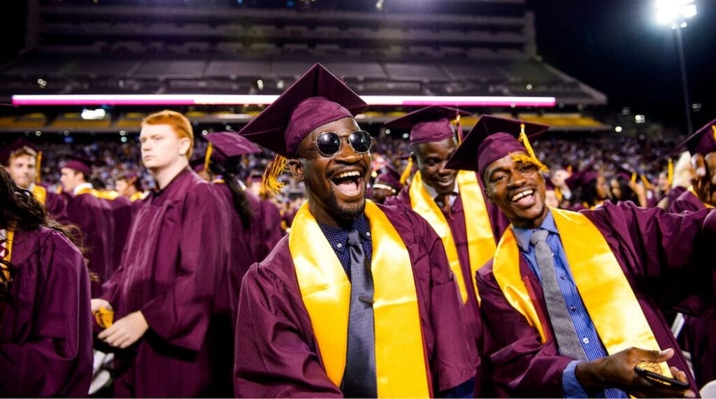 Two happy college students screaming at their graduation with a crowd of fellow graduates behind them