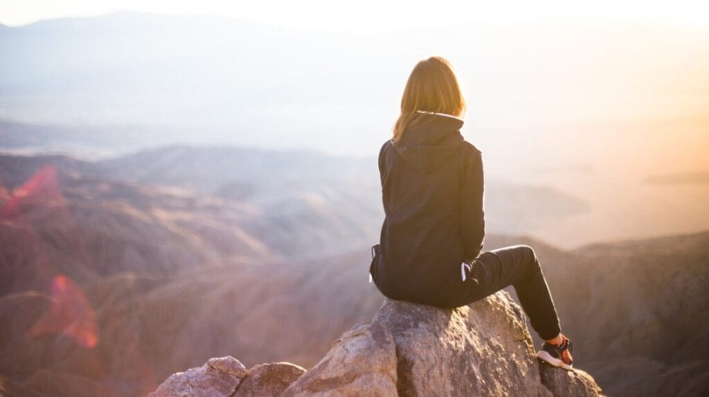 Person in dark clothing sitting on a mountain top looking at the sunset