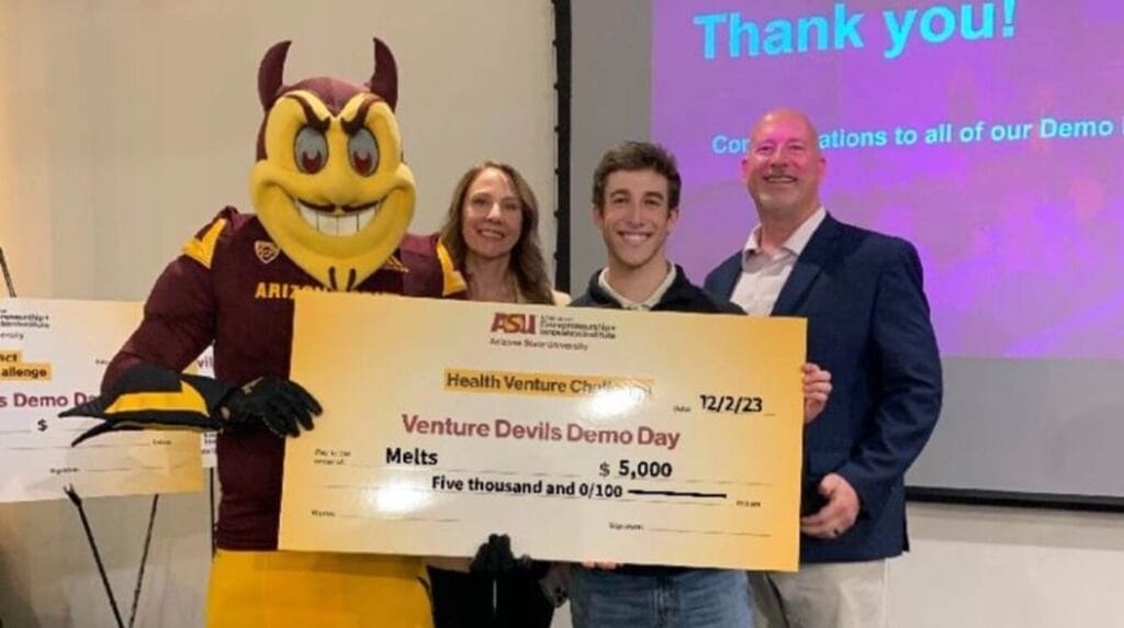 Three people and a mascot smiling and holding a large check at Venture Devils Demo day