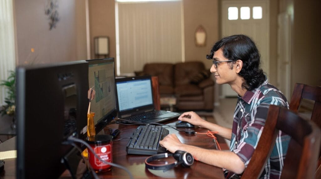 A person sitting at a home desk smiling at their computer screen