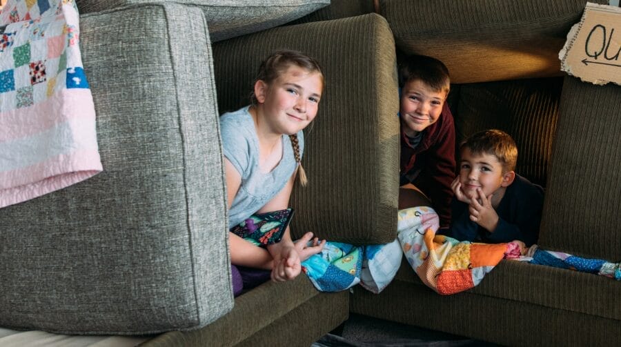 Group of three kids smiling and making forts with couch cushions