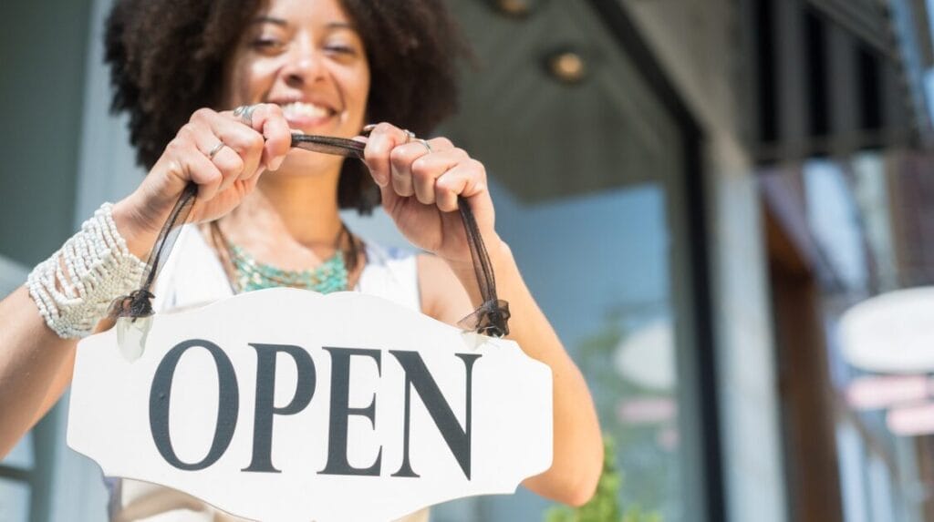A person holding an open sign in front of a retail sign