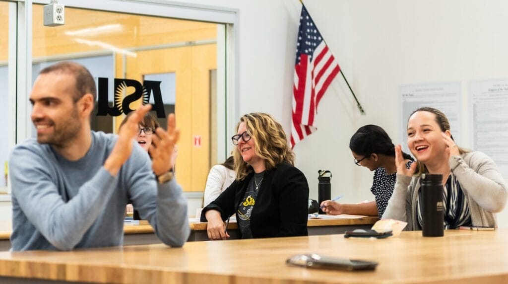 People sitting at wood tables smiling and clapping