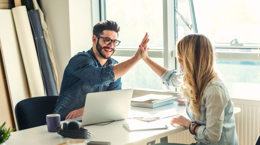 Two coworkers high fiving in their office