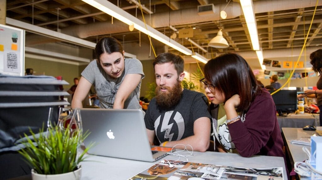 Three students working together at in an indoor innovation space looking at a laptop