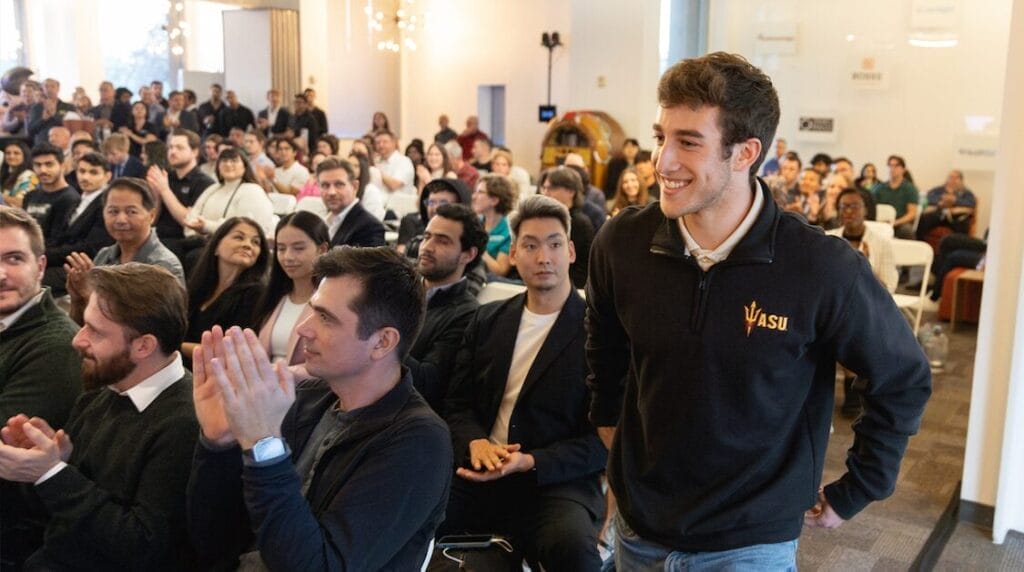 A crowd of people clapping for a young entrepreneur walking up to the stage