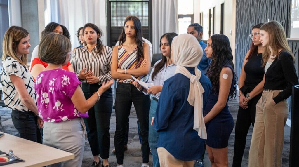 A small group of nursing students dressed in professional clothing standing and watching someone speak