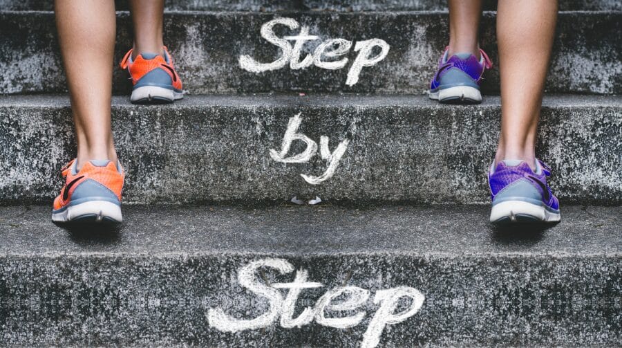 Two teenagers climbing stairs with ‘Step by Step’ painted on the steps