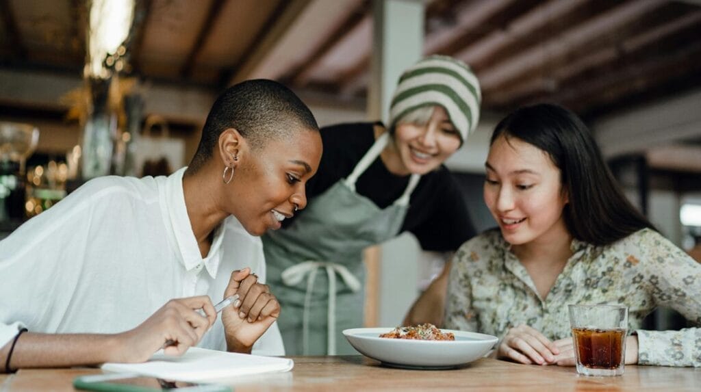 Two customers and the server smiling at their food at a restaurant