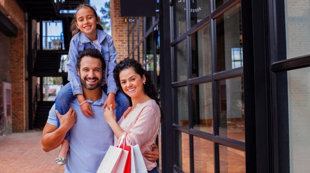A family smiling outside of a shopping mall with shopping bags