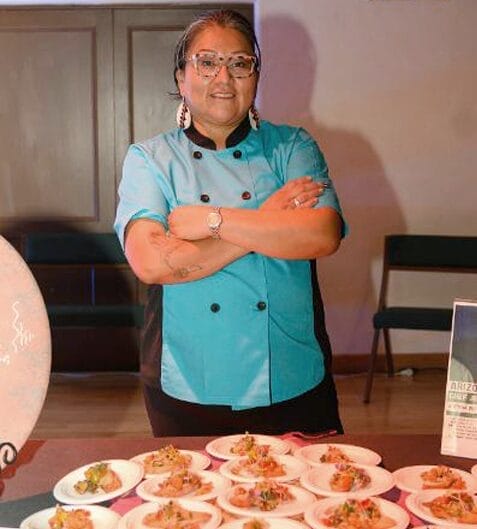 A chef standing behind a table of several plates of food 