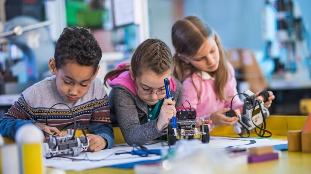 Three children sitting at a table and working on a robotics project