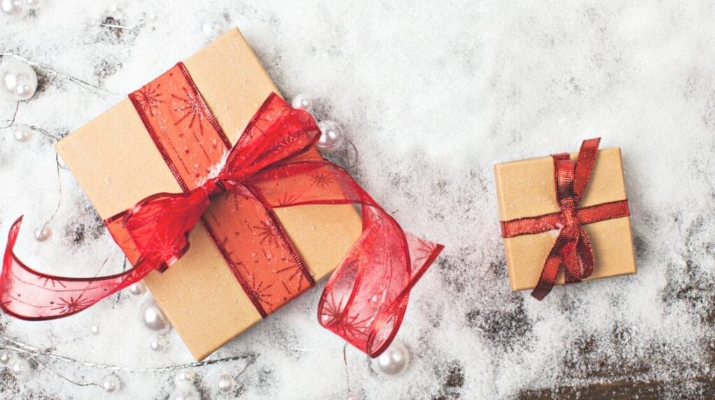 Two gift boxes with holiday theme bows on top of snow and pearls sprinkled around the gifts