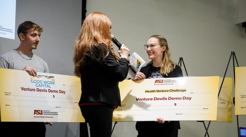 Two people holding large checks representing their win at Venture Devils Demo Day event