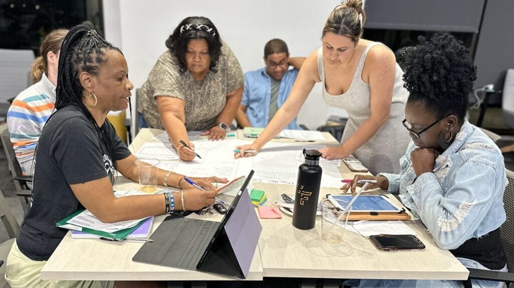 Four people standing over a table and writing on sticky notes at a Startup School event