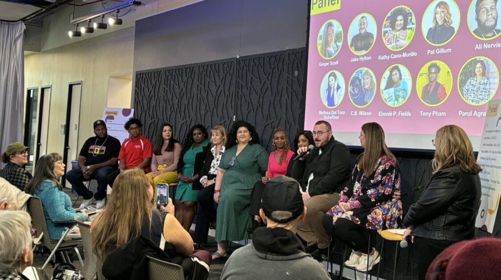 A group of ten authors speaking at an event to an audience.