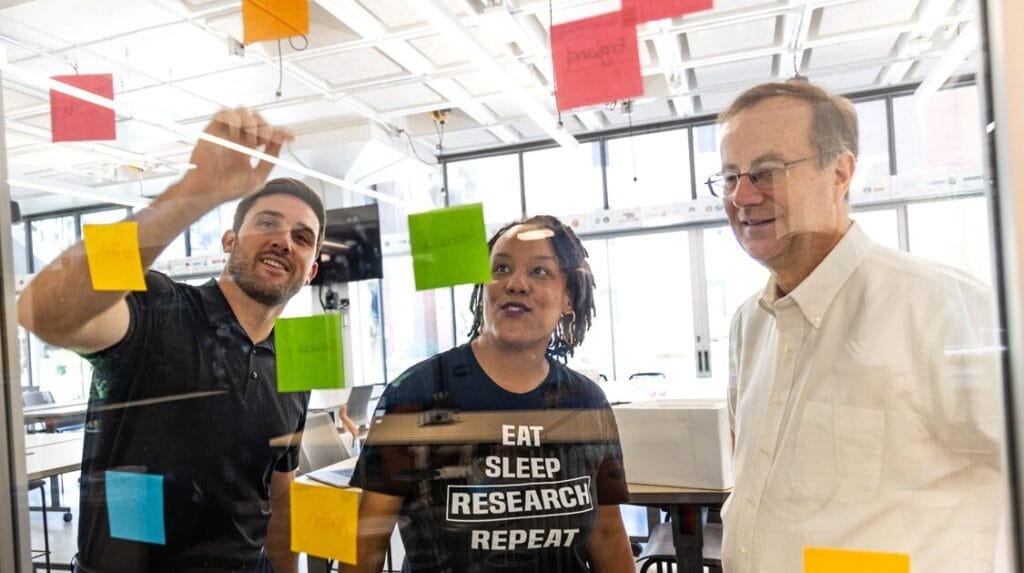 Three people collaborating and looking at sticky notes on a glass window