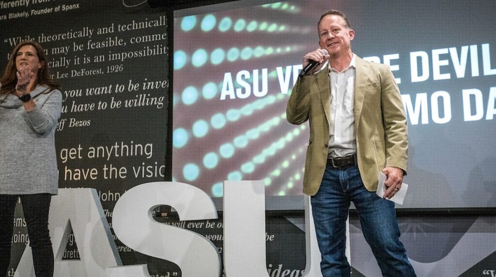 One person clapping and one person speaking into a microhpne on stage at Venture Devils Demo Day