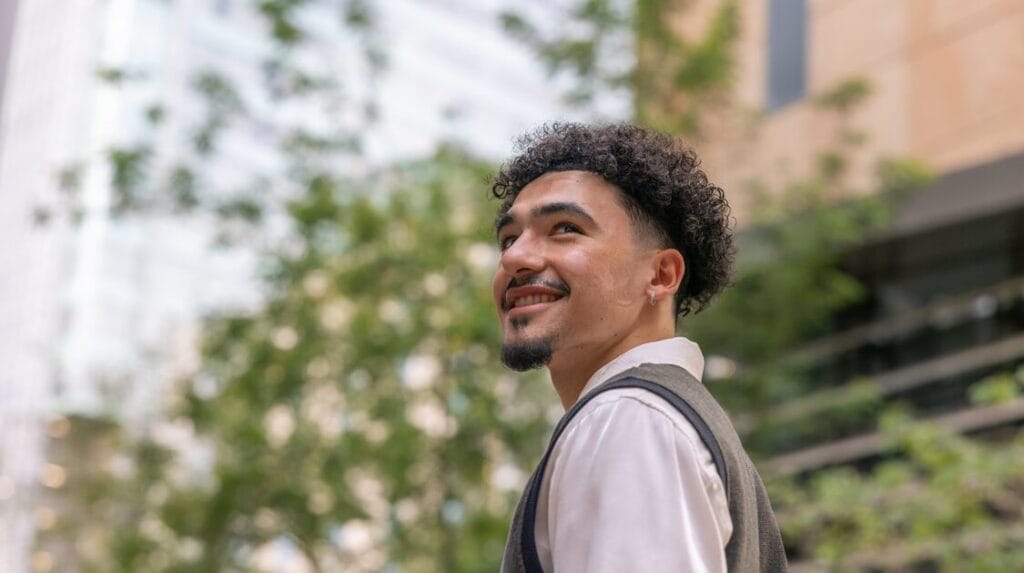 A young person standing outside and smiling on the ASU campus with trees and buildings in the background