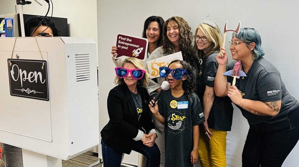 Five people and a child using and wearing fun props at a professional event and smiling at the camera