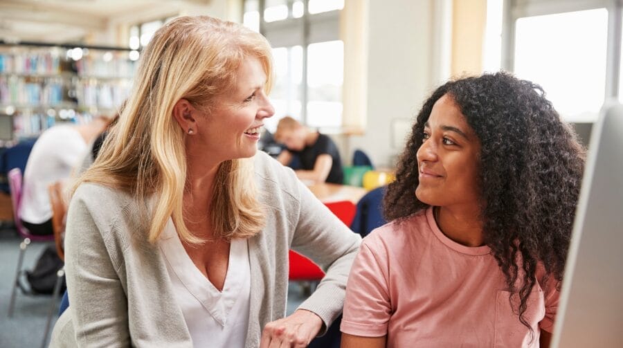 A teenager in a classroom smiling at a teacher sitting next to her.