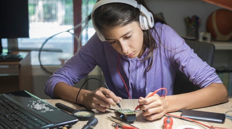 A teenager sitting, wearing headphones and working on a circuit board.
