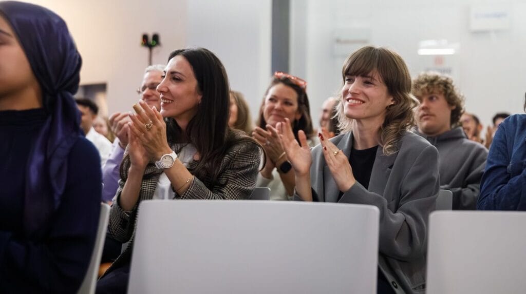 Two people in an audience clapping and smiling at a pitch event