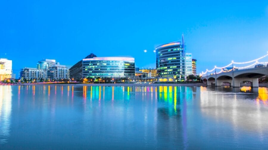 A view of buildings in the City of Tempe set behind a river with a reflection of city lights on the water.
