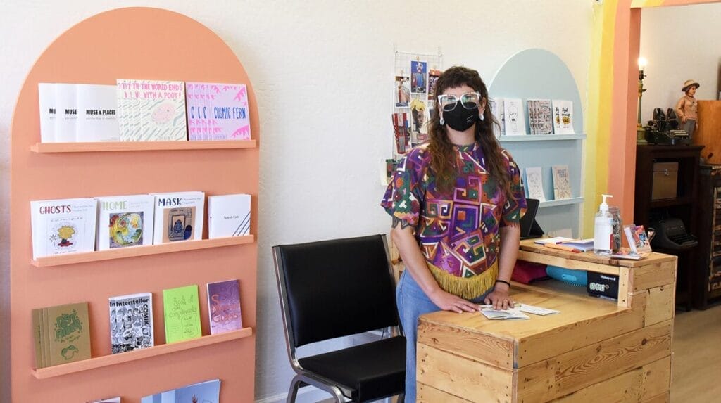 A person standing behind a wood counter in a retail store with books on shelves in the background.