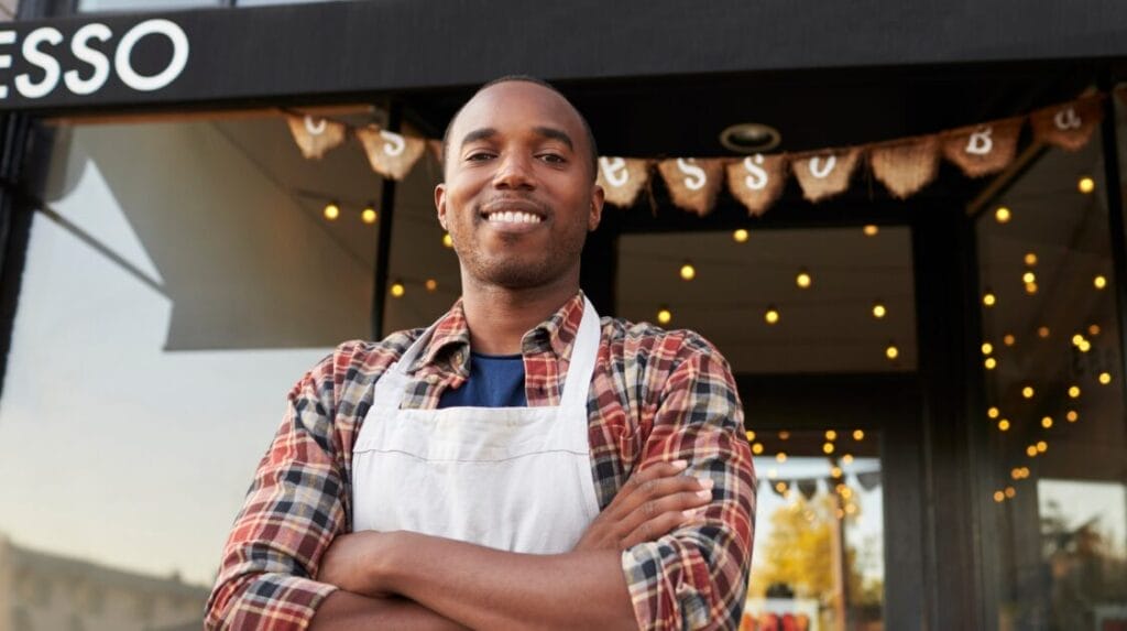 A retail store owner standing in front of their store and smiling